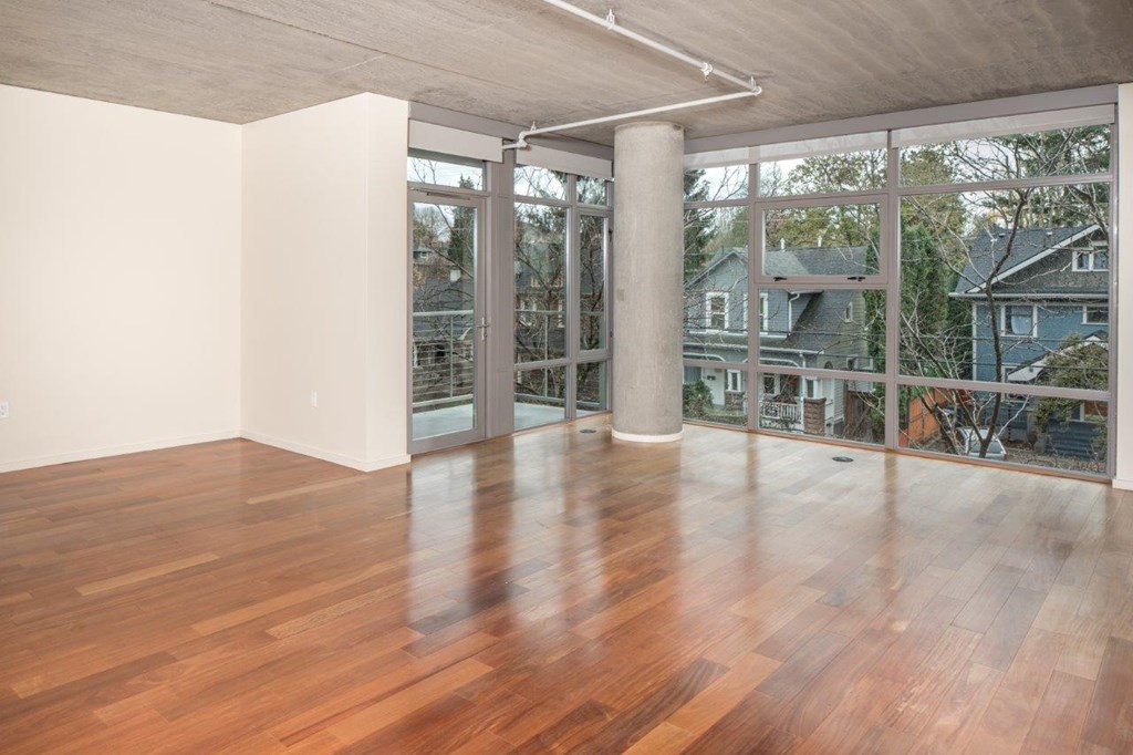 A room with wooden floors and a balcony with a view of houses.