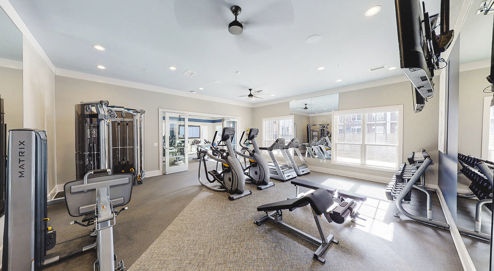 Fitness center with cardio machines and weights with an outdoor view from the large windows.