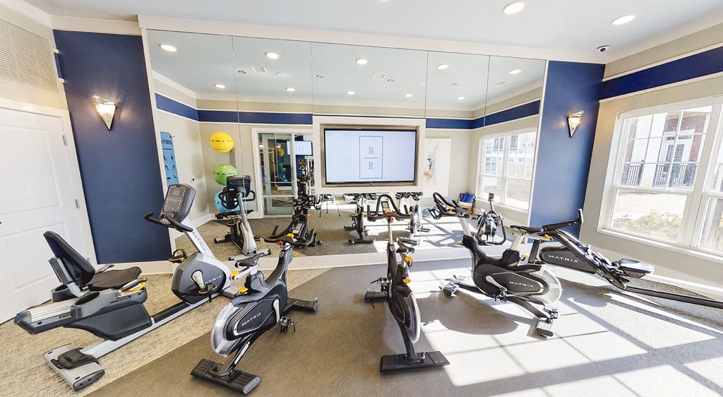 Five cardio machines in front of a large mirror in the resident fitness center.