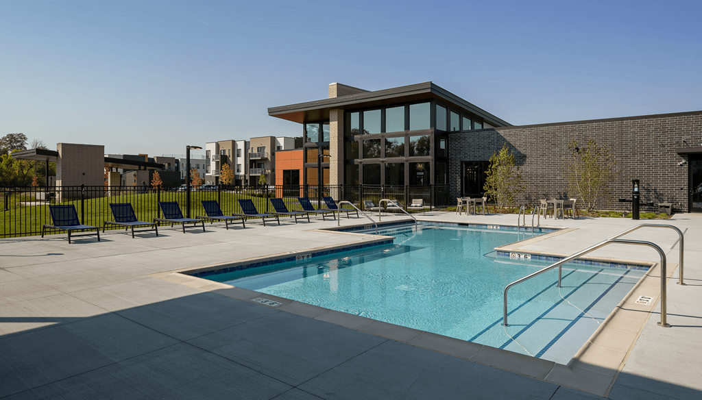a swimming pool with blue chairs and a building in the background