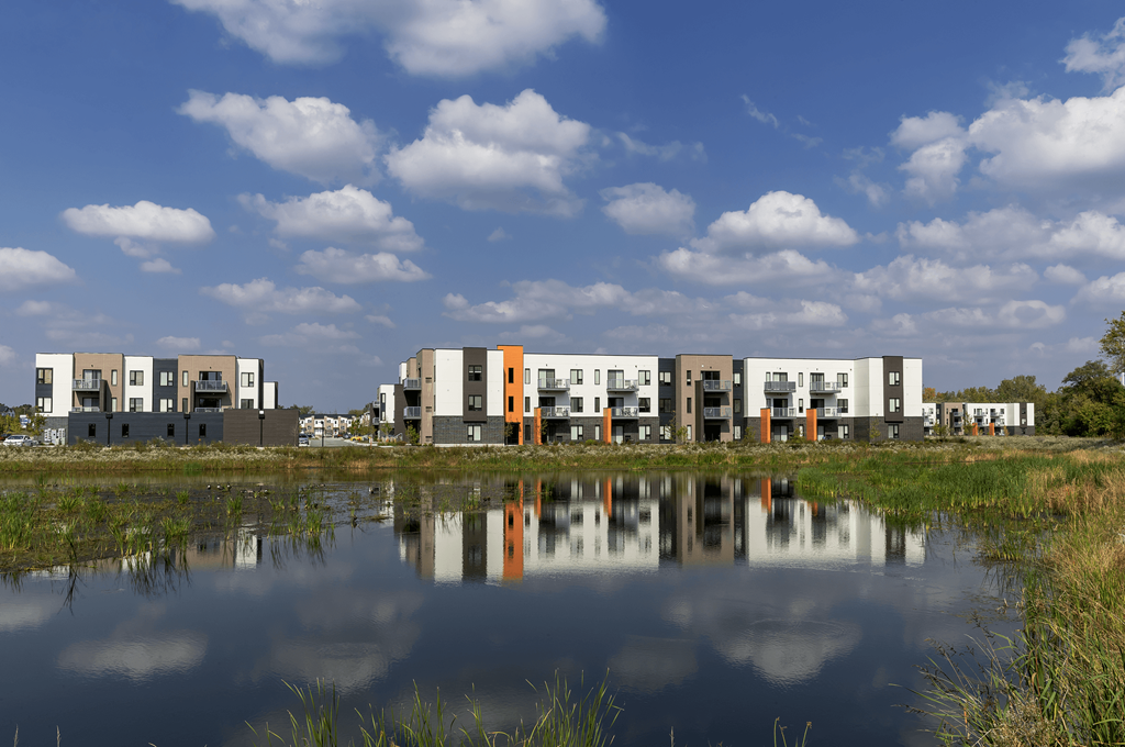 a row of apartment buildings are reflected in a body of water