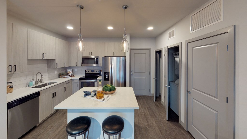 Kitchen area with 2 hanging lights, a kitchen island, and stainless steel appliances. 