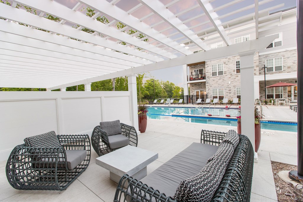 3 chairs under a pergola with a view of the pool.