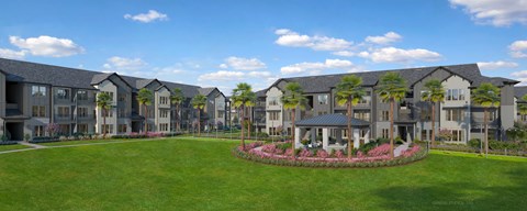 A large building complex with a green lawn in front and a circular flower bed in the middle.