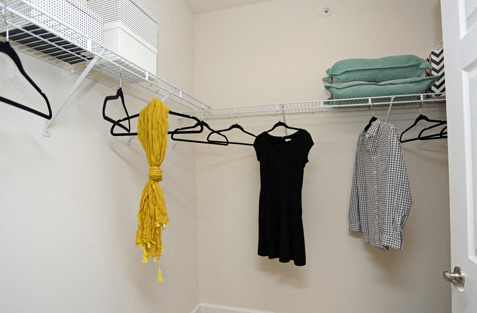 a closet with a rack with clothes and a dress and a yellow scarf