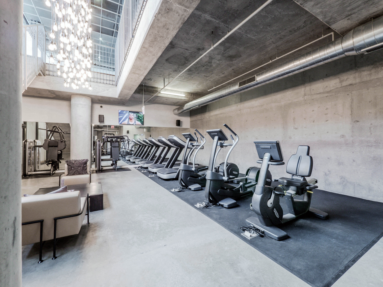 Stairs leading to the fitness center with multiple workout equipment and a mounted TV. 
