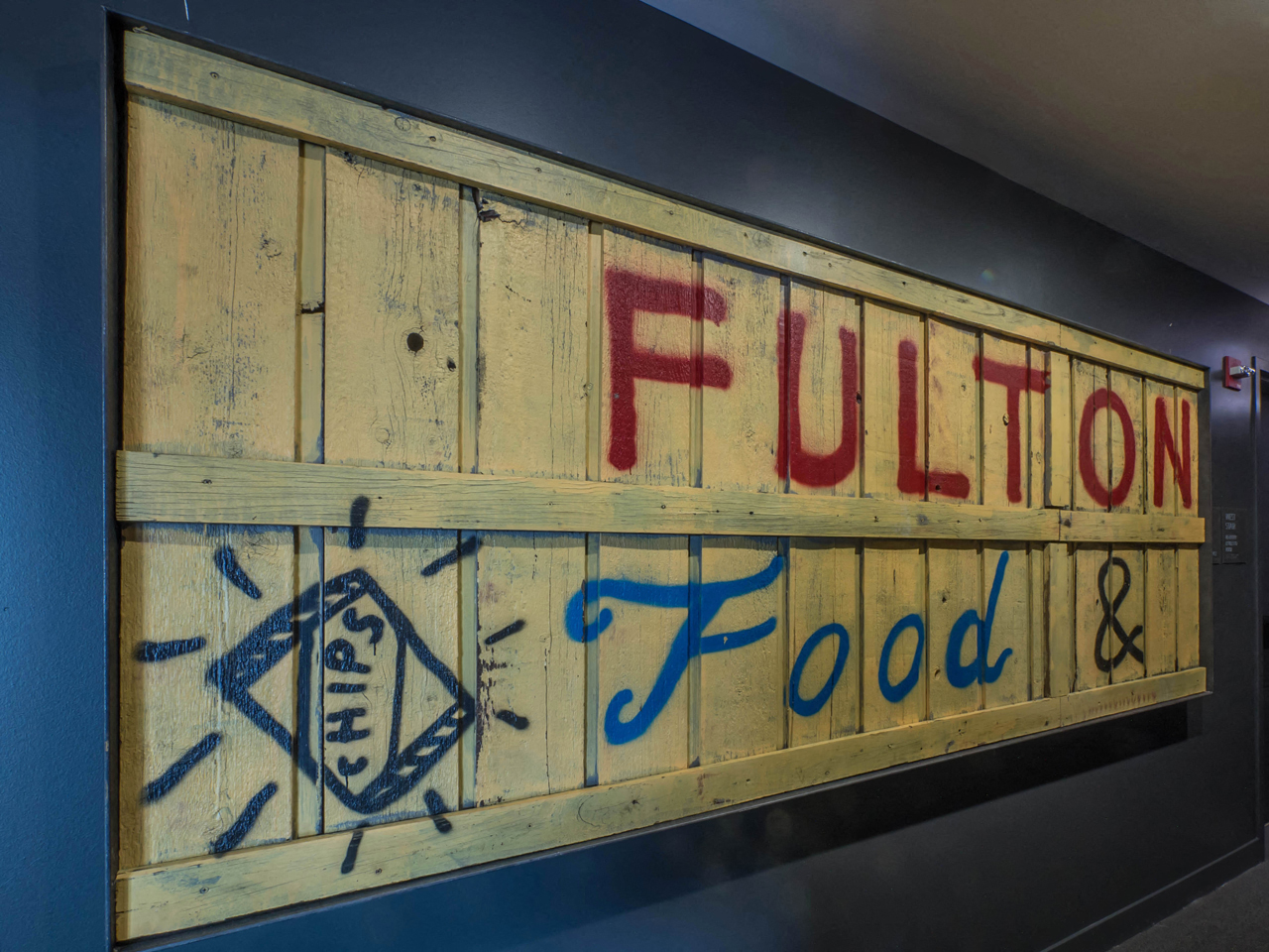 Wooden sign with "Fulton Food" painted on it.