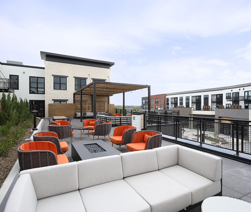 a rooftop patio with a white couch and orange chairs
