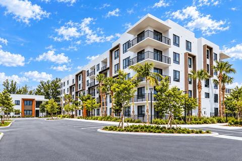A modern multi-story residential building with a parking lot in front.