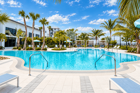 A swimming pool surrounded by palm trees and a white building.
