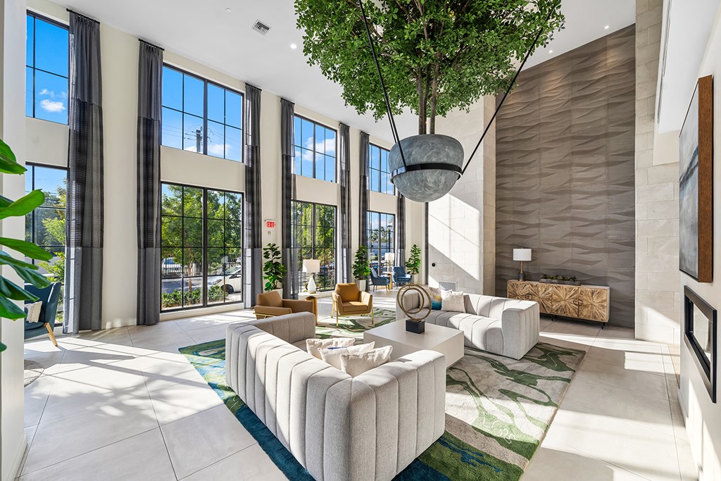 a spacious living room with large windows and a tree in the middle