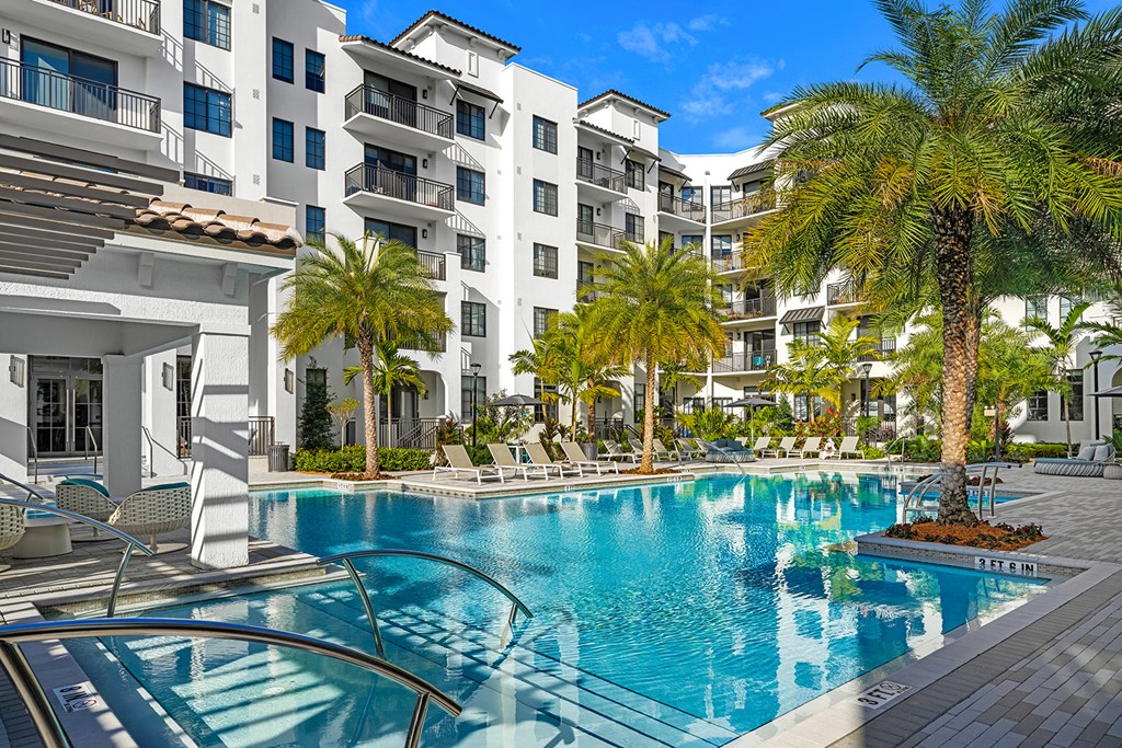 a swimming pool with palm trees in front of an apartment building