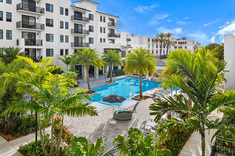 a swimming pool with palm trees in front of an apartment building