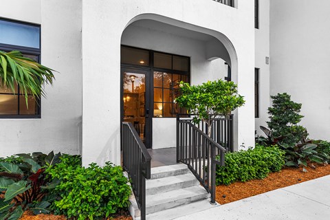 the front entrance of a building with stairs and plants