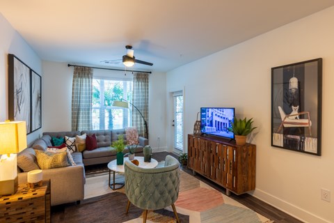 A living room with a couch, a chair, a coffee table, a television, and a window with curtains.