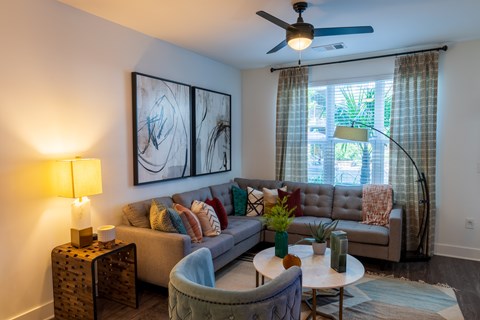 A living room with a grey couch, a table with a vase and a plant on it, and a painting on the wall.