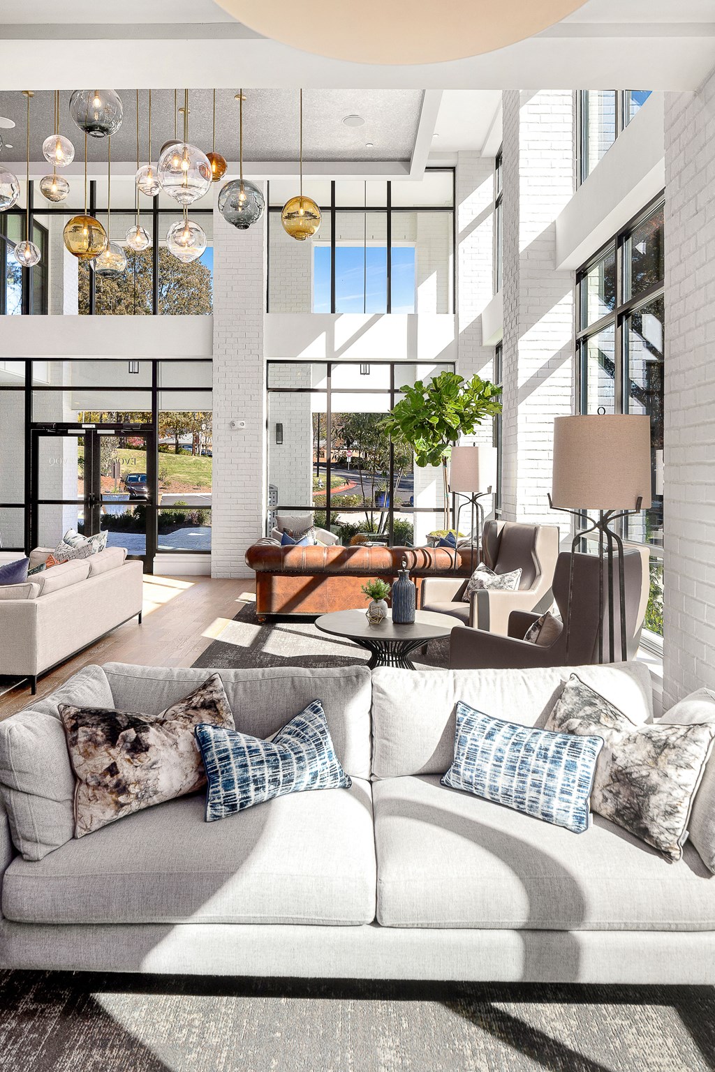 A white couch with pillows is in the foreground of a bright room with a large window.