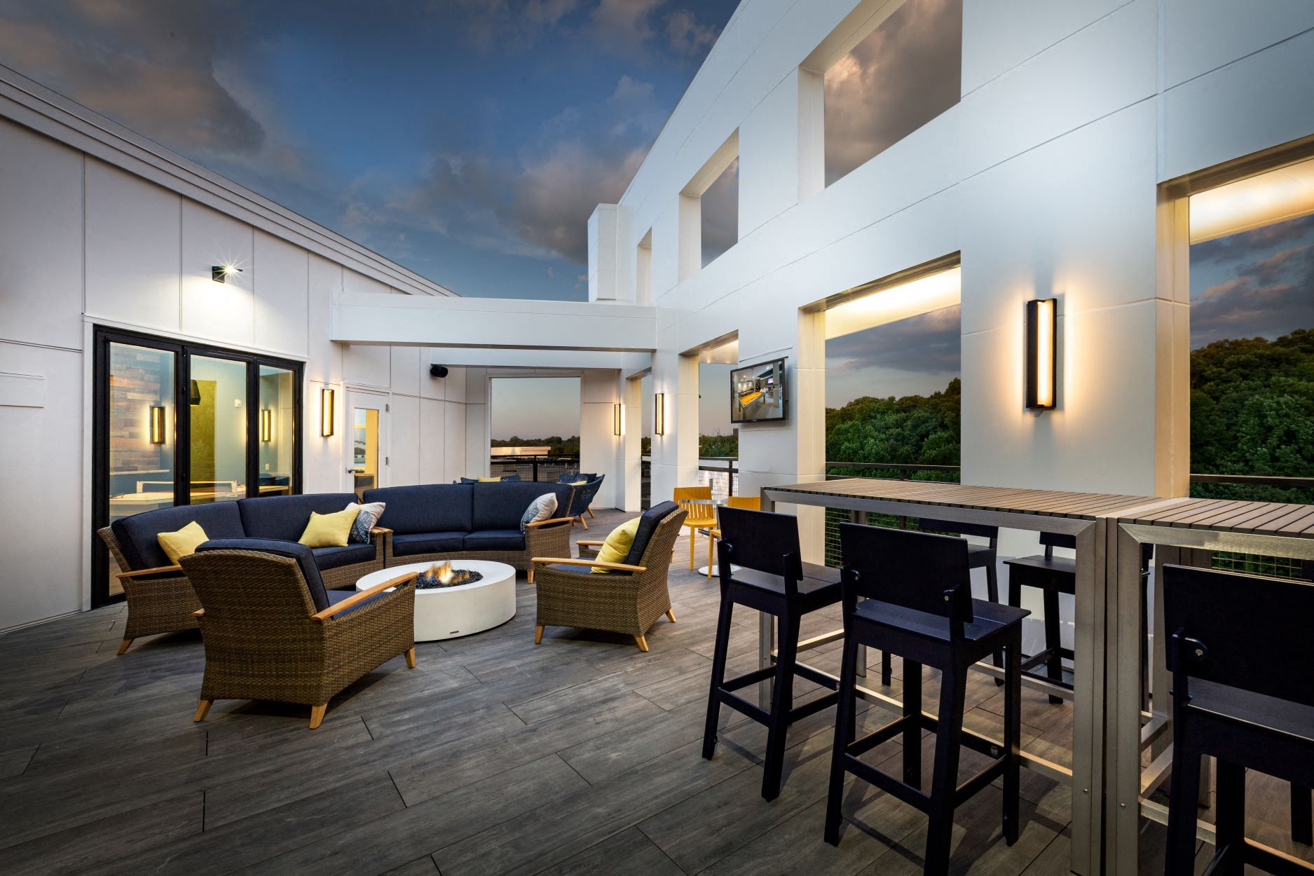 Rooftop sky lounge with chairs around a fire pit and a bar with stools.
