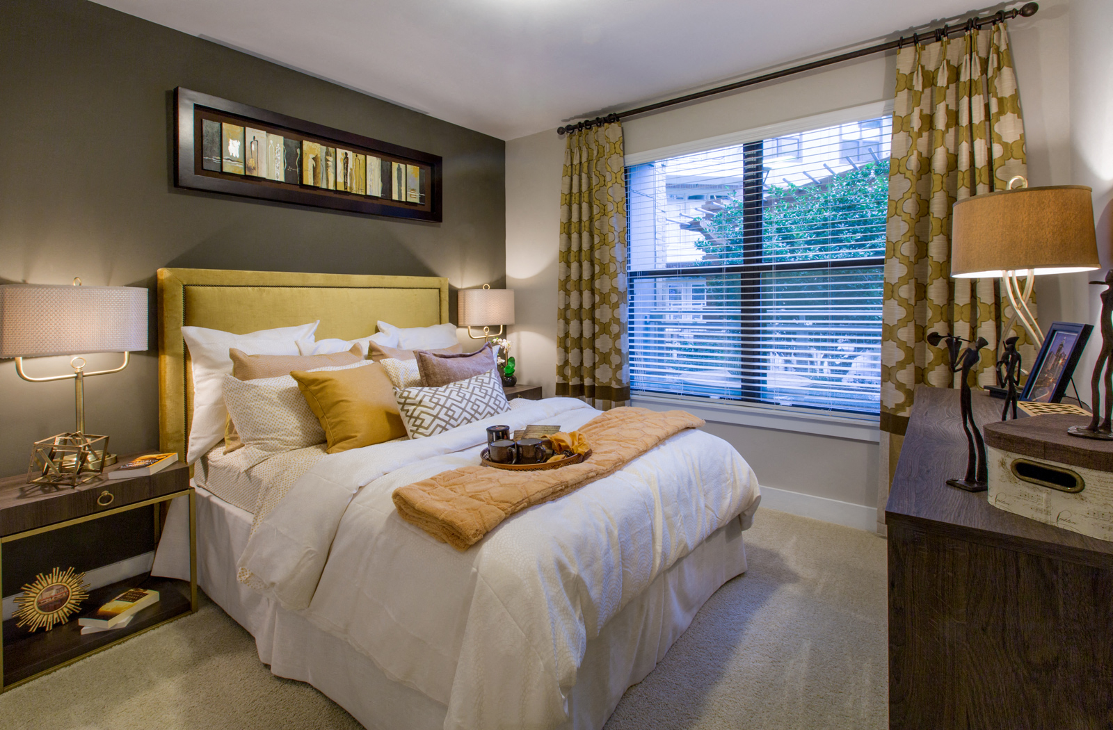 Bed in the middle of two nightstands with a window view facing the outdoors. 