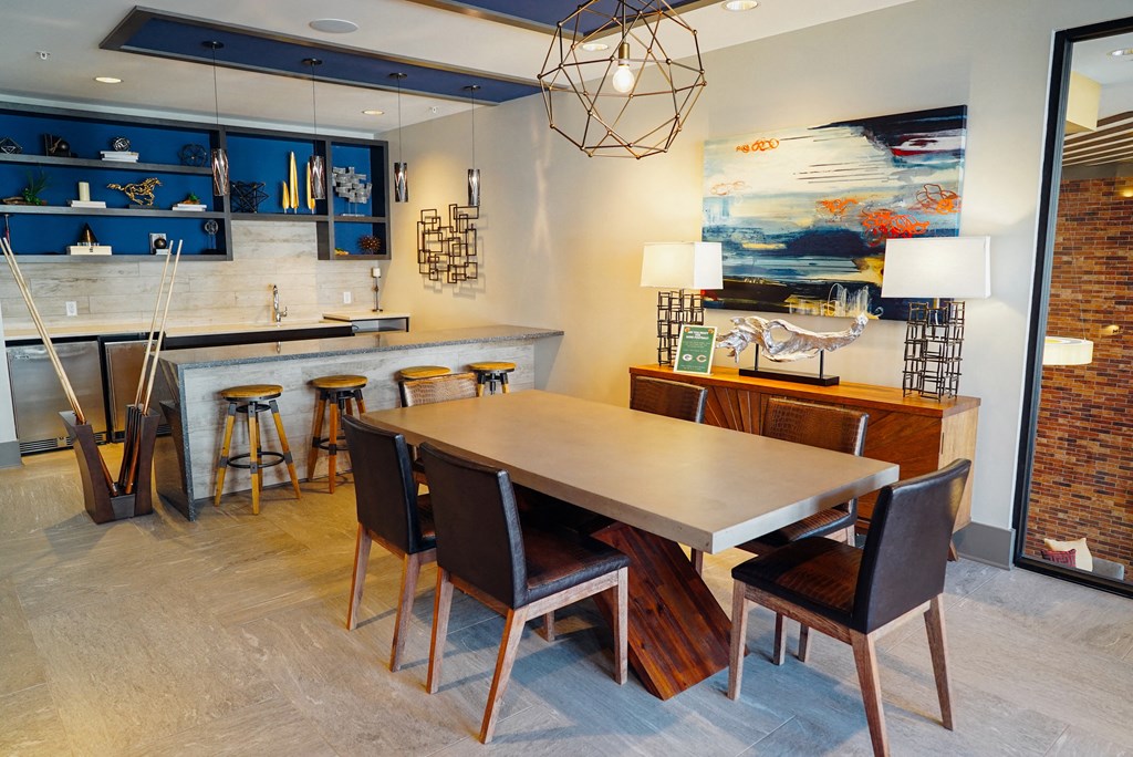 Decorated community area with table and chairs, kitchen island, and kitchen space including a mini fridge.