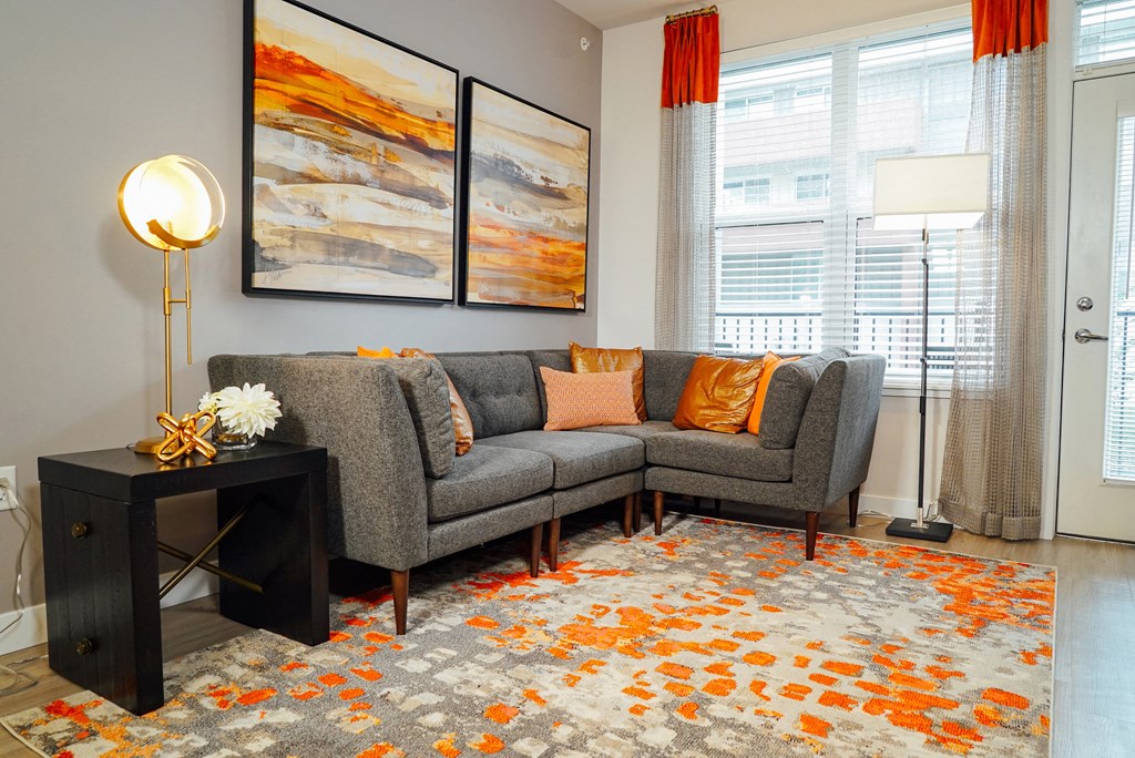 Living room space with a corner couch, large rug, and entry way to balcony. 