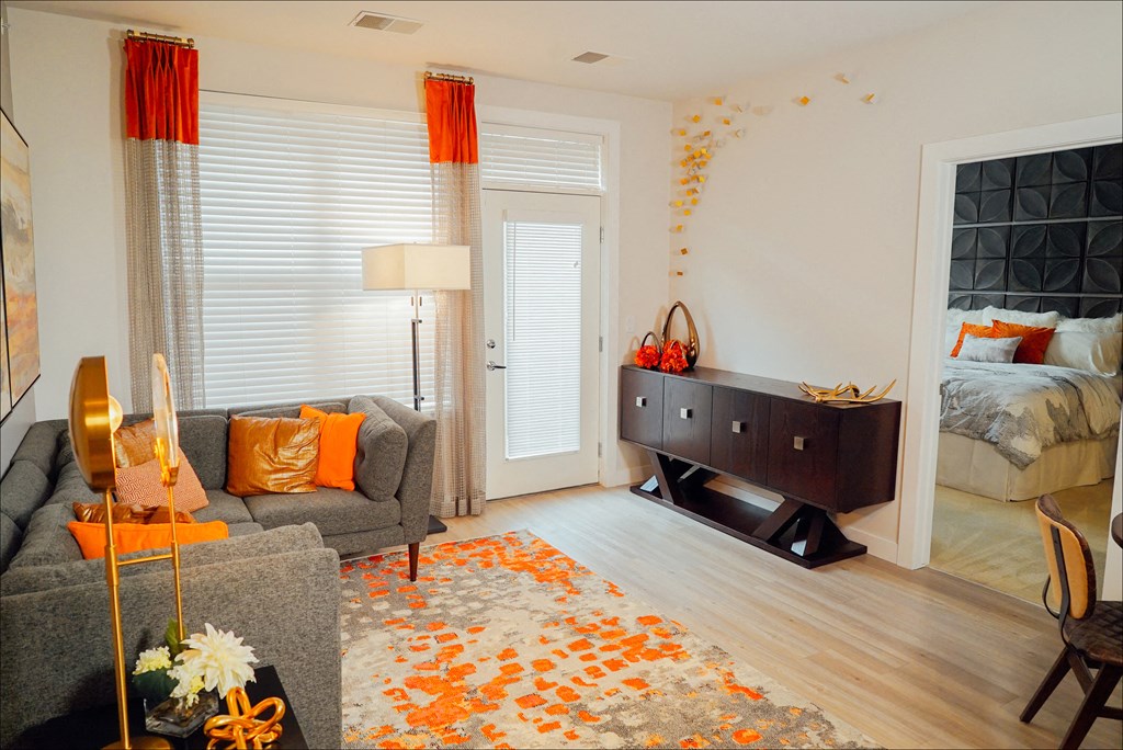 Living room space with a corner couch, large rug, and large window, with doorway to the bedroom. 