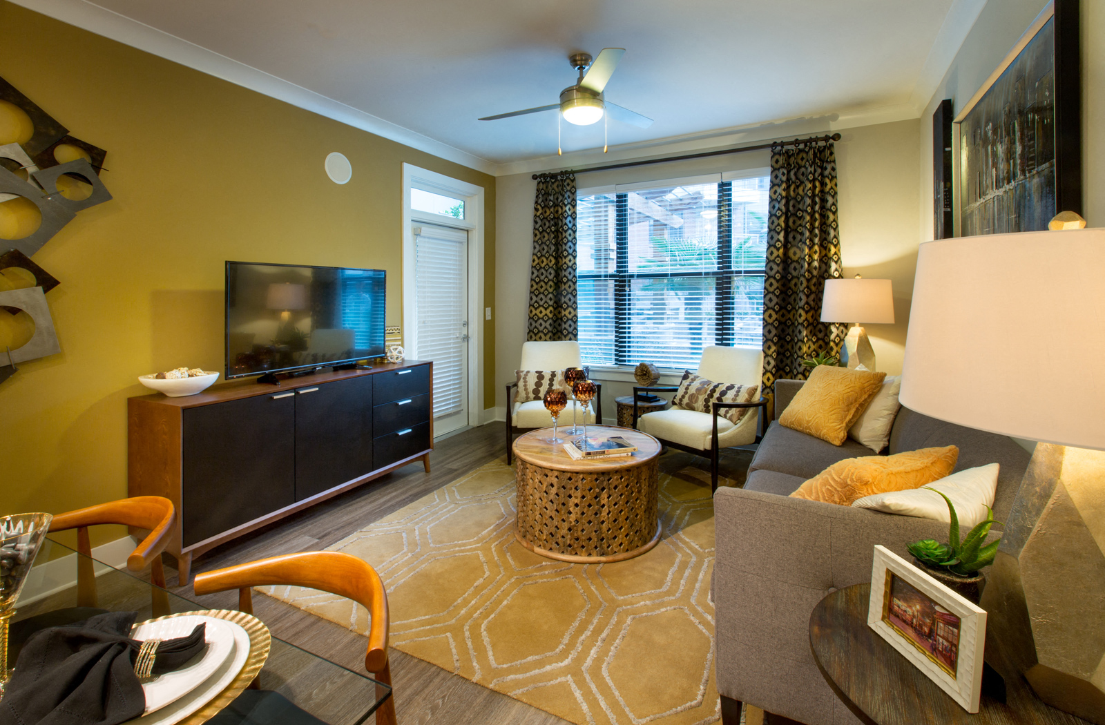 Furnished living room area with wooden floors and large windows facing the pool area. 