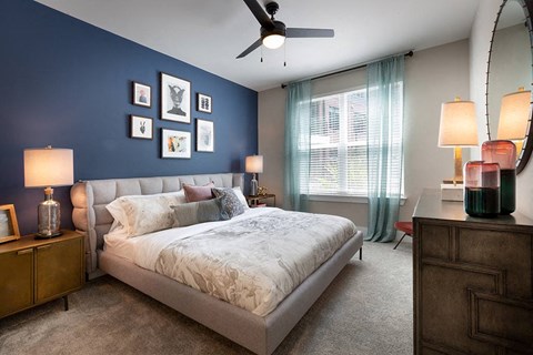 Carpeted bedroom with a queen sized bed, ceiling fan, and large window.