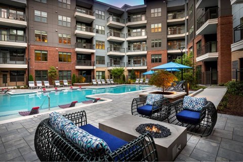 A pool area with chairs and a table with a fire pit in front of apartment buildings.