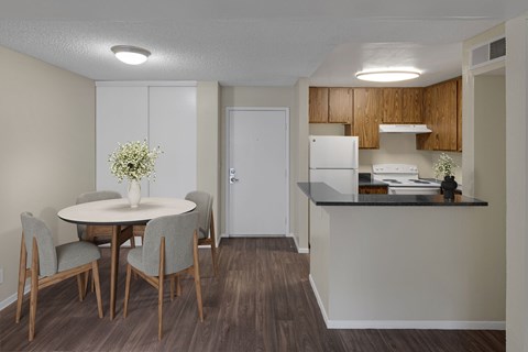 A kitchen with a table and chairs in the foreground and a refrigerator and cabinets in the background.
