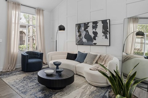 A modern living room with a white couch, a black chair, and a large abstract painting on the wall.