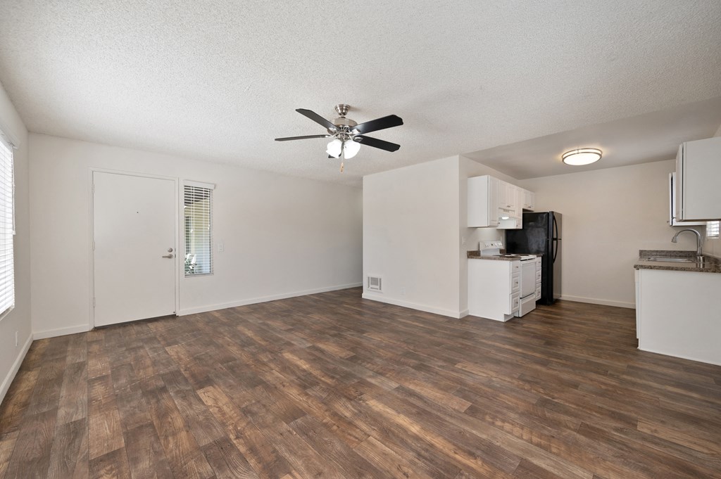 an empty living room with a ceiling fan and a kitchen