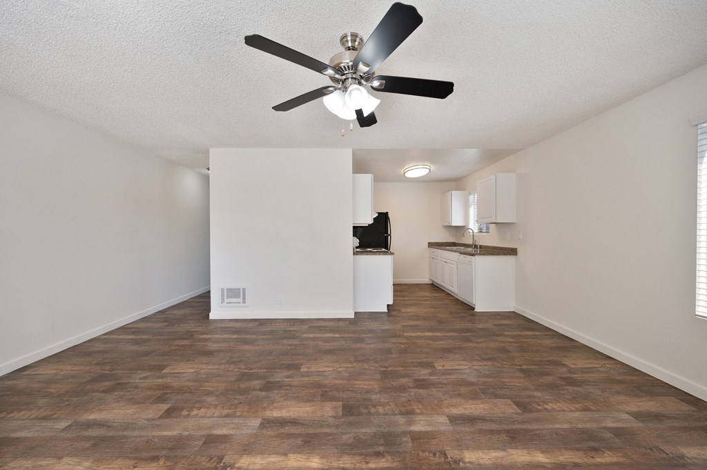 an empty living room with a ceiling fan and a kitchen