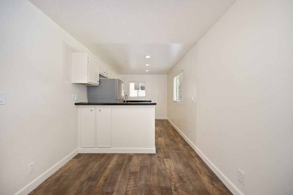 the living room and kitchen of a manufactured home with white walls and wood flooring