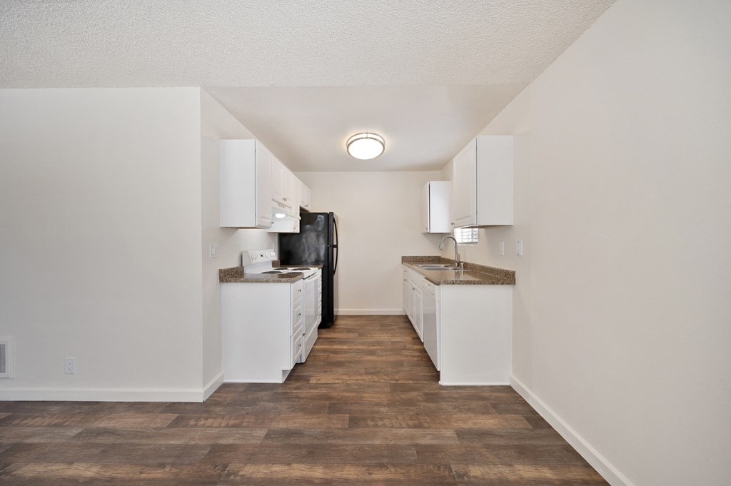 the living room and kitchen of an apartment with white walls and wood flooring
