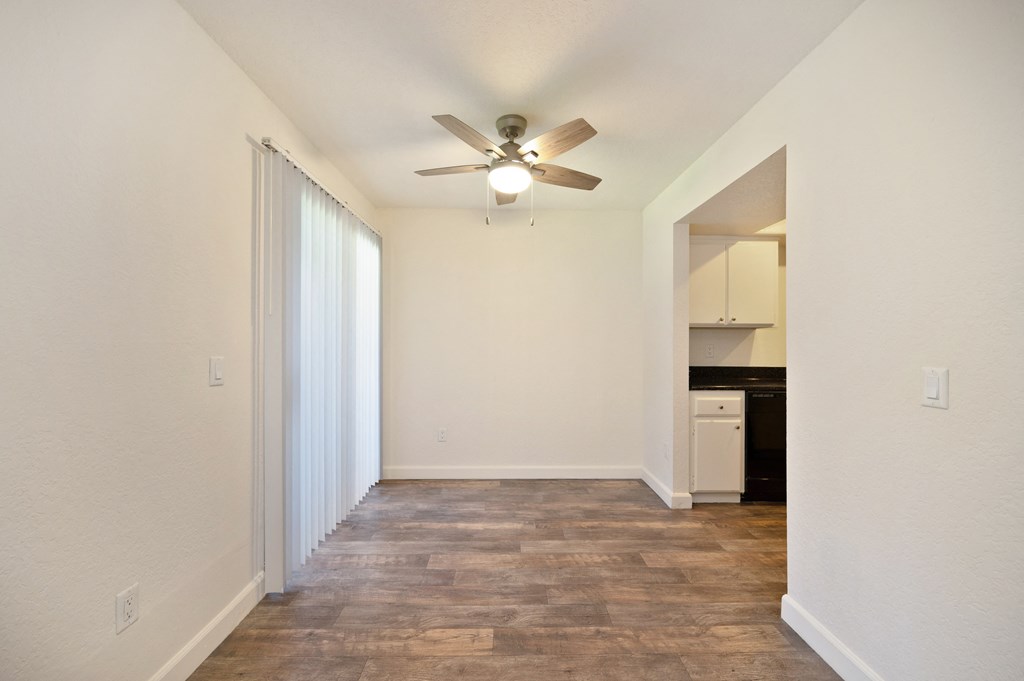 an empty living room with a ceiling fan and a kitchen