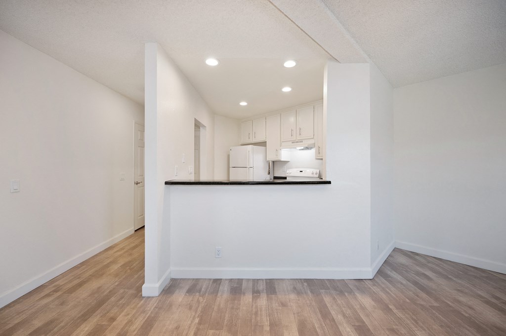 the living room and kitchen of an apartment with white walls and wood flooring