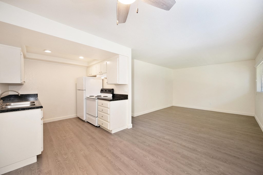 an empty kitchen and living room with white appliances and wood flooring