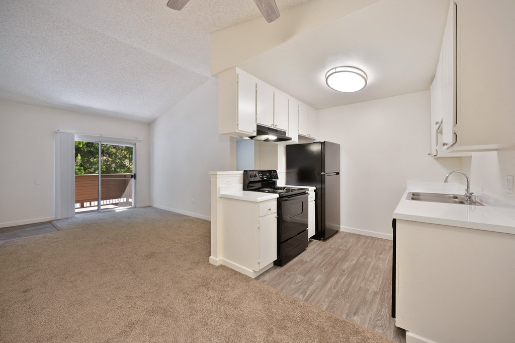 an empty living room with a kitchen with a stove and refrigerator