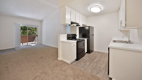 A kitchen area with a black refrigerator, white cabinets, and a window with a view of trees.