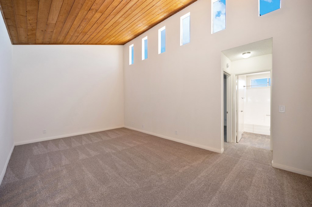 an empty living room with white walls and a wooden ceiling