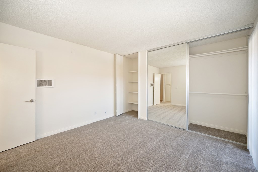 an empty bedroom with mirrored closet doors and a carpeted floor