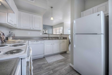A white refrigerator stands in a kitchen with white cabinets and a white stove.