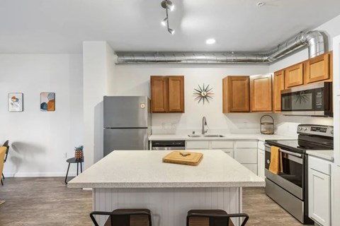 A kitchen with a table and chairs in the foreground and a refrigerator, microwave, oven, and sink in the background.