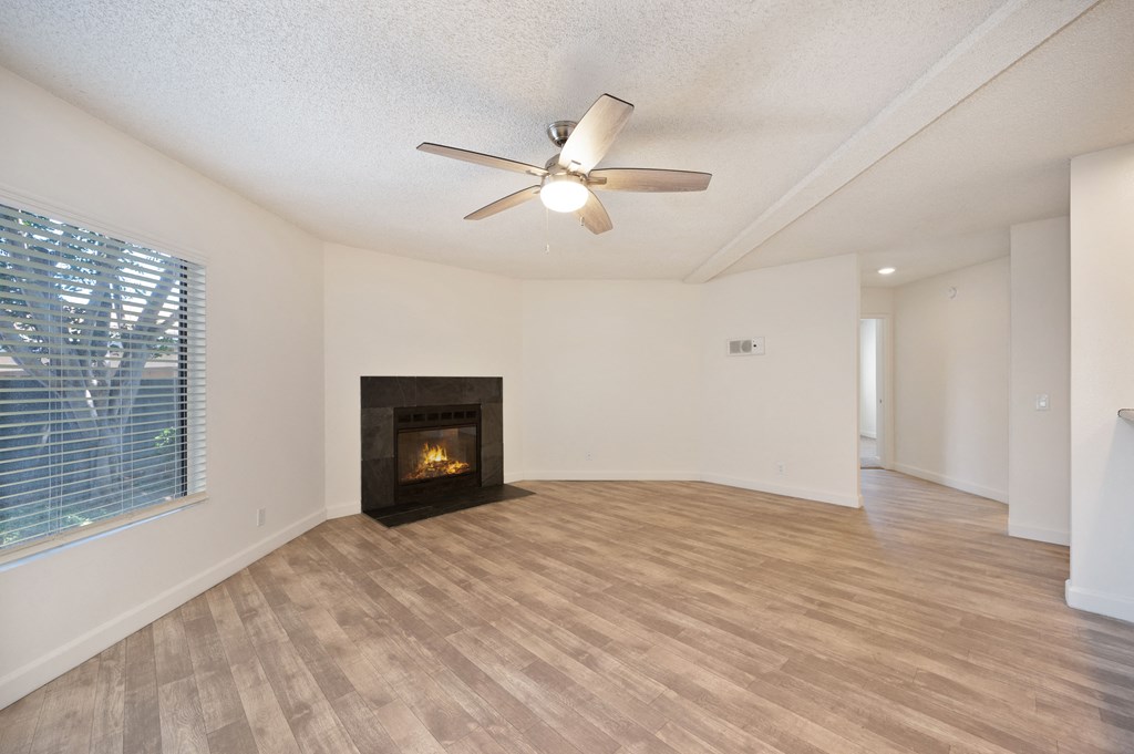 an empty living room with a fireplace and a ceiling fan
