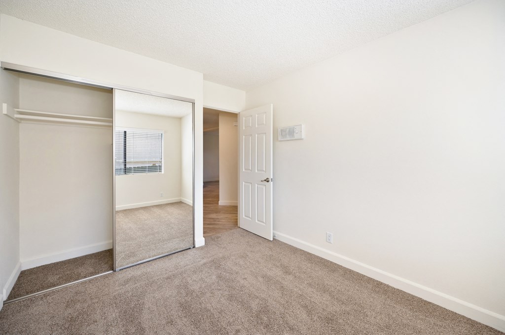 an empty bedroom with a mirrored closet and a door to a hallway