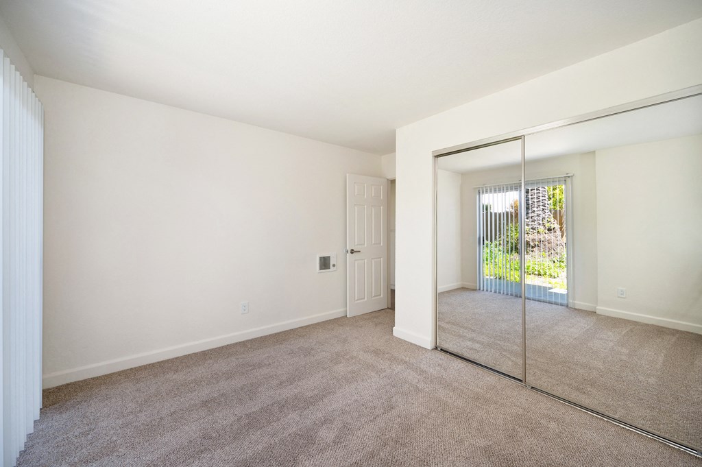 an empty living room with a mirrored closet and a door to a patio