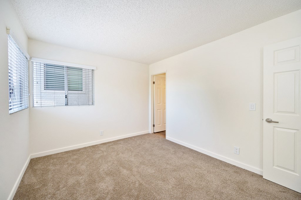a spacious bedroom with white walls and carpeting and a door to the bathroom