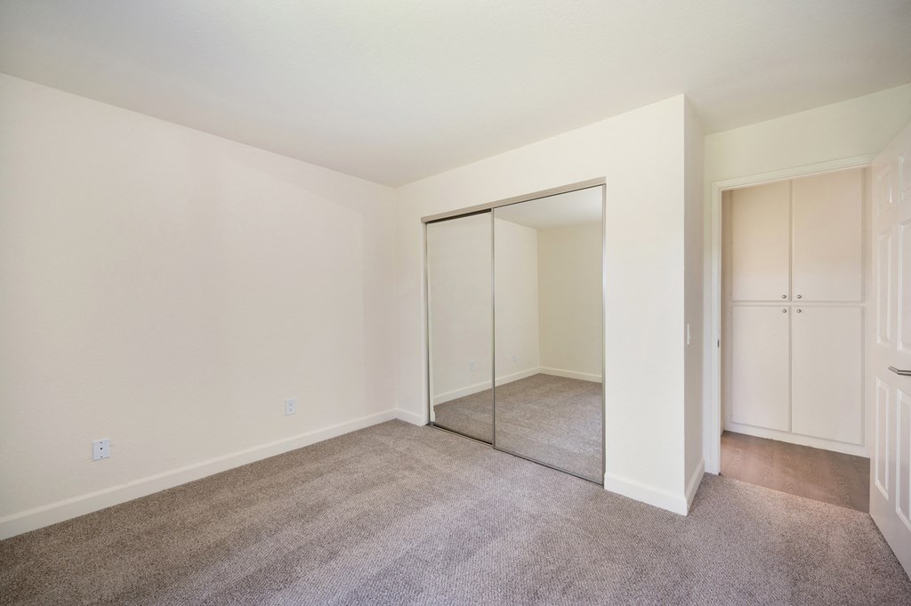 a bedroom with carpet and a closet with a mirrored door