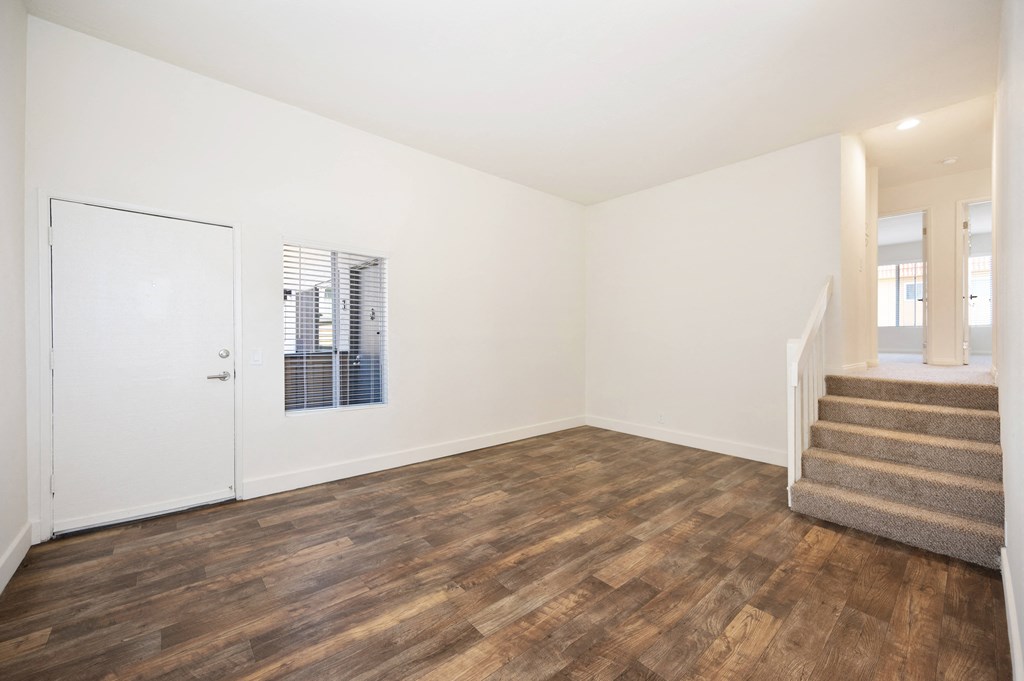 a living room with white walls and wood flooring and a staircase